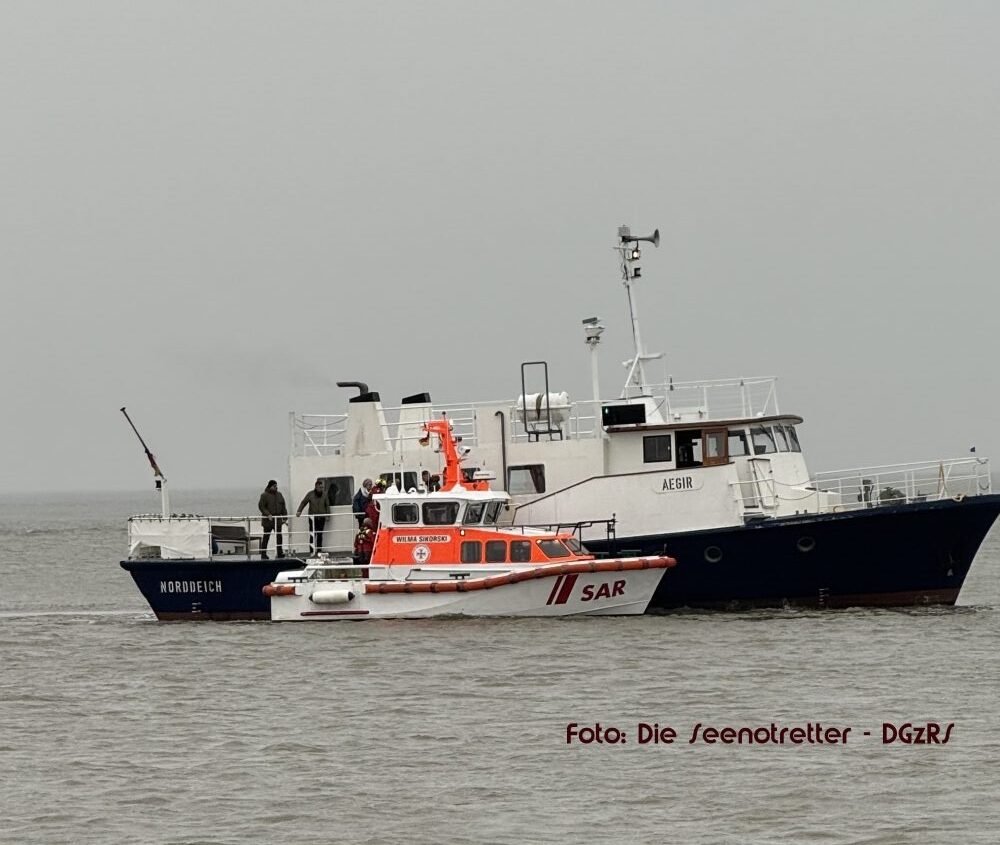 Mit dem Seenotrettungsboot WILMA SIKORSKI der DGzRS übernehmen die Seenotretter acht Menschen von einem festgekommenen Bestattungsschiff. Foto: Die Seenotretter – DGzRS